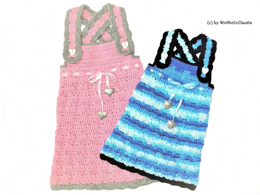 Zwei gehäkelte Kinderkleider: rosa mit grauen, gekreuzten Trägern und Herzknöpfen; blau gestreift mit schwarzen Trägern und Herzanhängern.