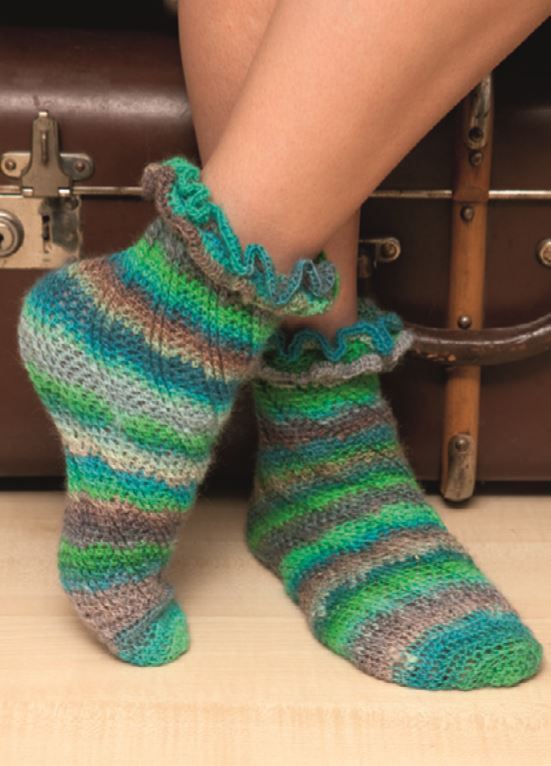 Gestreifte, gehäkelte Damensocken mit Rüschenbund auf hellem Holzfußboden vor einem braunen Koffer.
