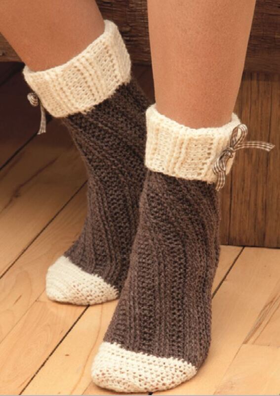 Nahaufnahme braun-beiger gehäkelter Damensocken mit umgeschlagenem Bündchen und Schleifen auf Holzboden