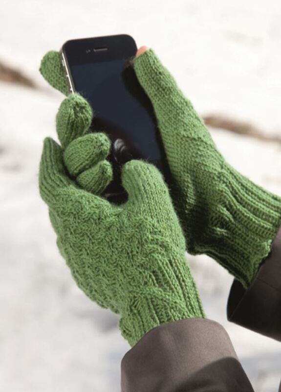 Hände in grünen gestrickten konvertierbaren Handschuhen bedienen ein Smartphone vor verschneiter Kulisse.