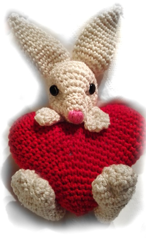 Cremefarbener gehäkelter Hase mit langen Ohren hält ein rotes Herz