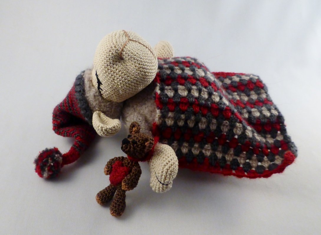 Gehäkeltes schlafendes Bärchen mit Bommelmütze, Mini-Teddy mit Herz und rot-grauer Decke