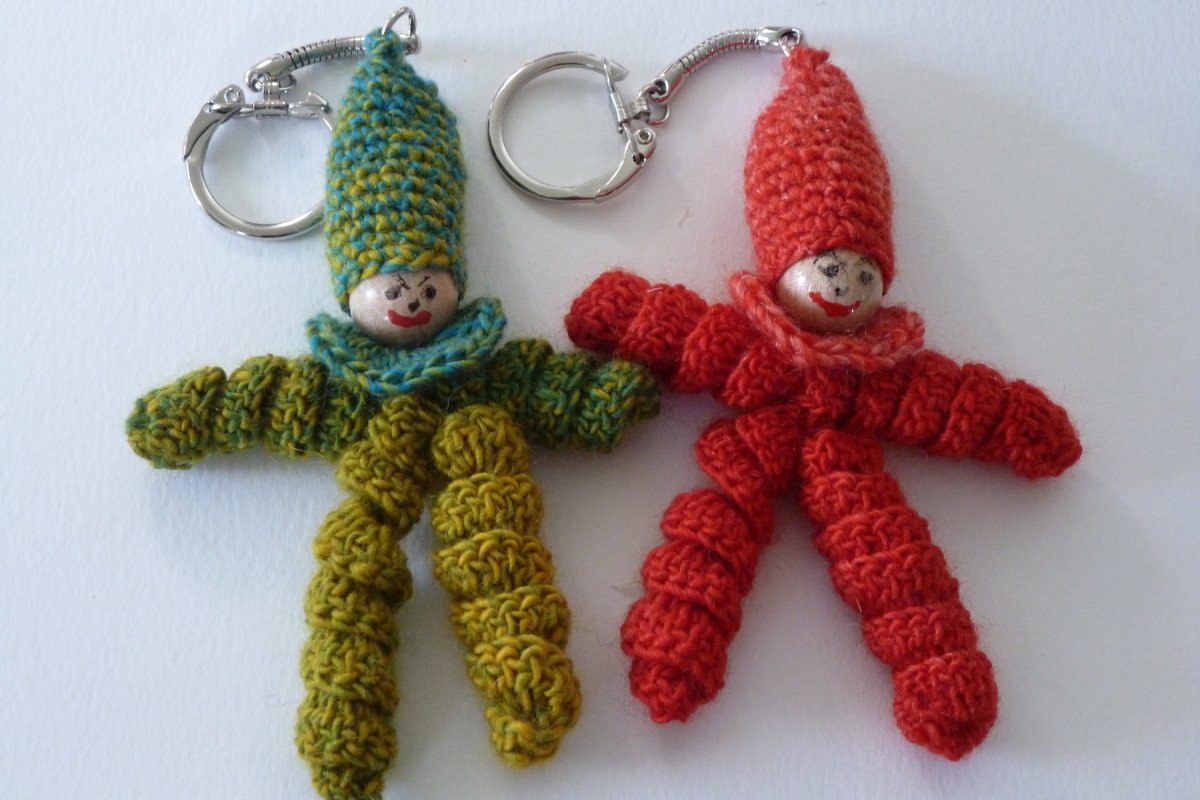 Zwei farbige Häkelpüppchen-Schlüsselanhänger mit spitzen Mützen, bemalten Holzperlenköpfen und Metallringen
