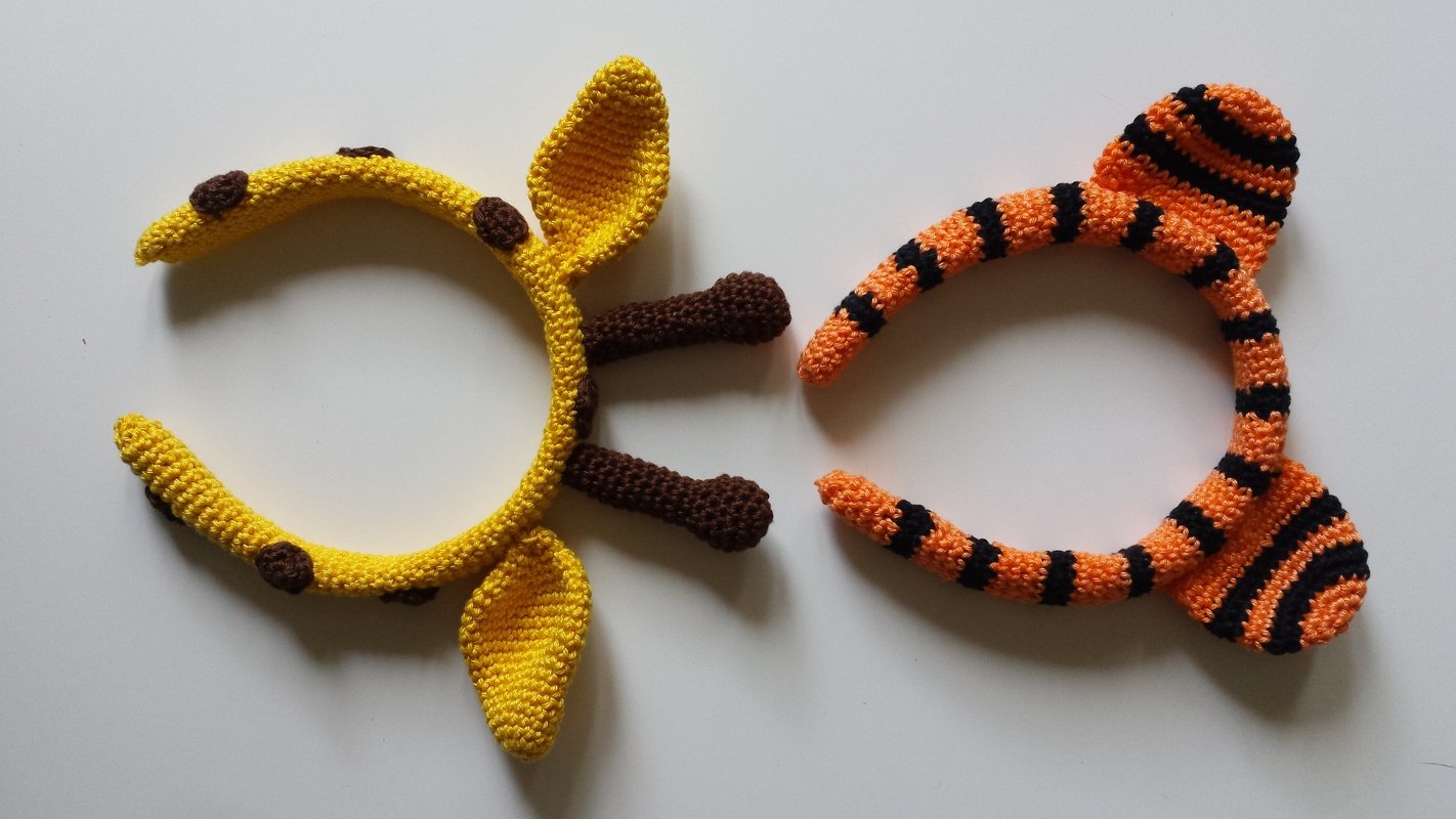Zwei gehäkelte Haarreifen: gelbe Giraffe und orange-schwarz gestreifter Tiger auf weißem Hintergrund.