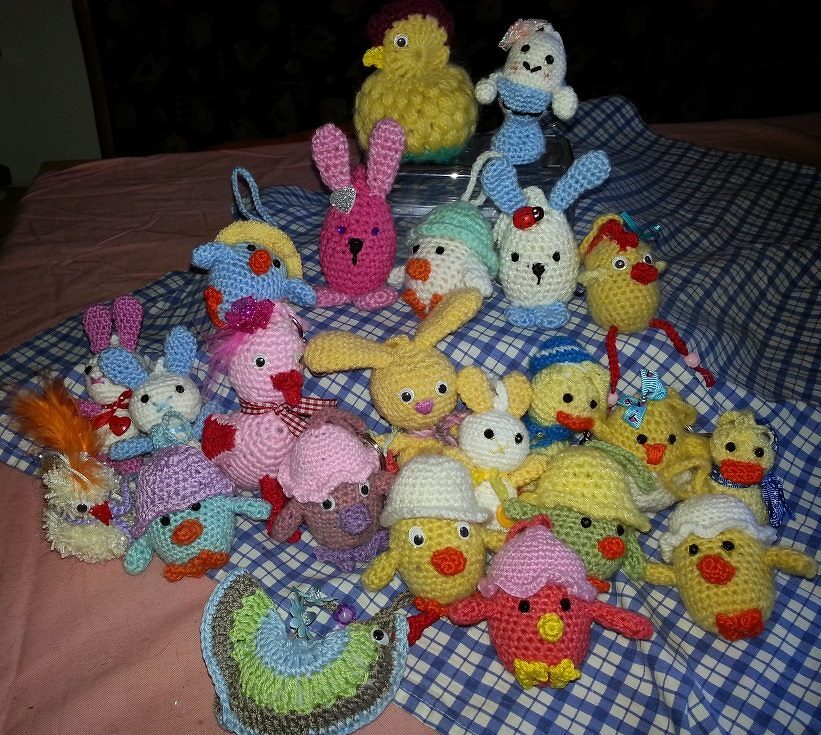 Viele gehäkelte Osterfiguren – Hasen, Küken und Enten – auf blau-weiß kariertem Stoff