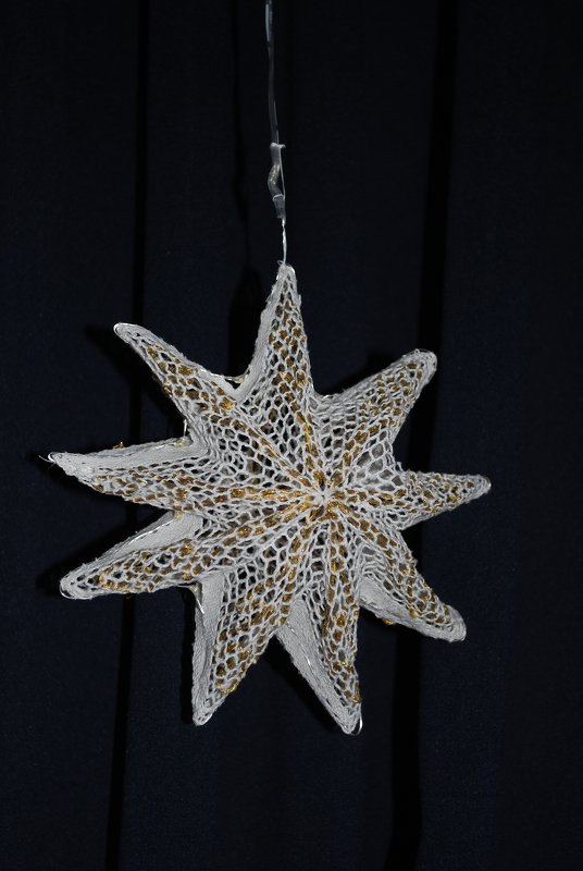 Hängender mehrzackiger Papierstern in Weiß mit goldfarbenen Akzenten vor dunklem Hintergrund