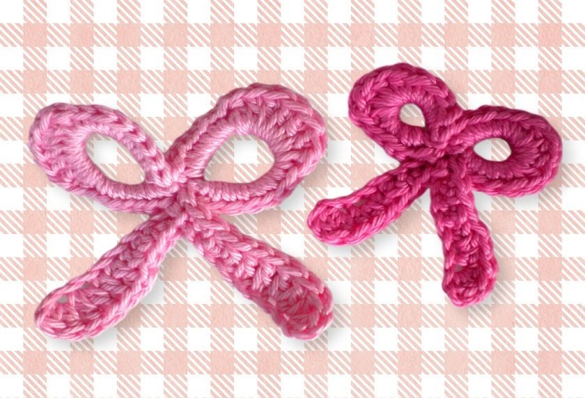 Zwei gehäkelte rosa Schleifen-Applikationen, eine hellrosa, eine dunkelrosa, auf kariertem Stoff