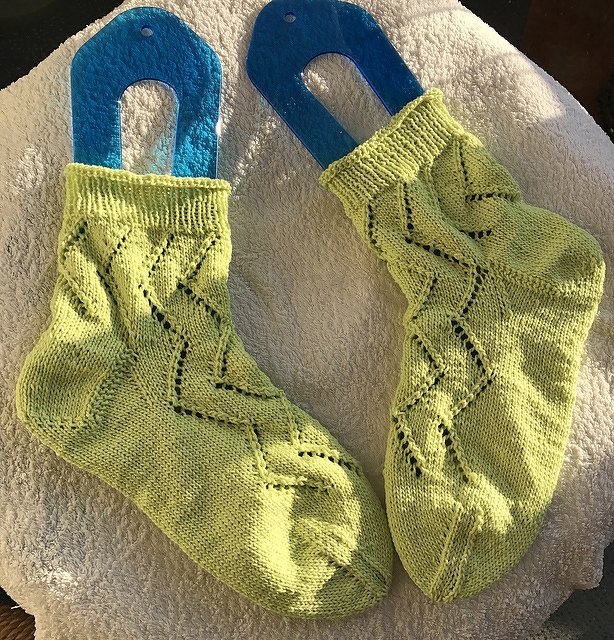 Lindgrüne handgestrickte Socken mit Zickzack‑Lochmuster auf blauen Sockenformern