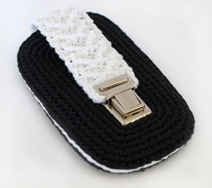 Schwarz-weißes gehäkeltes Utensilo mit Zopfmuster und metallischem Schnappverschluss auf hellem Hintergrund