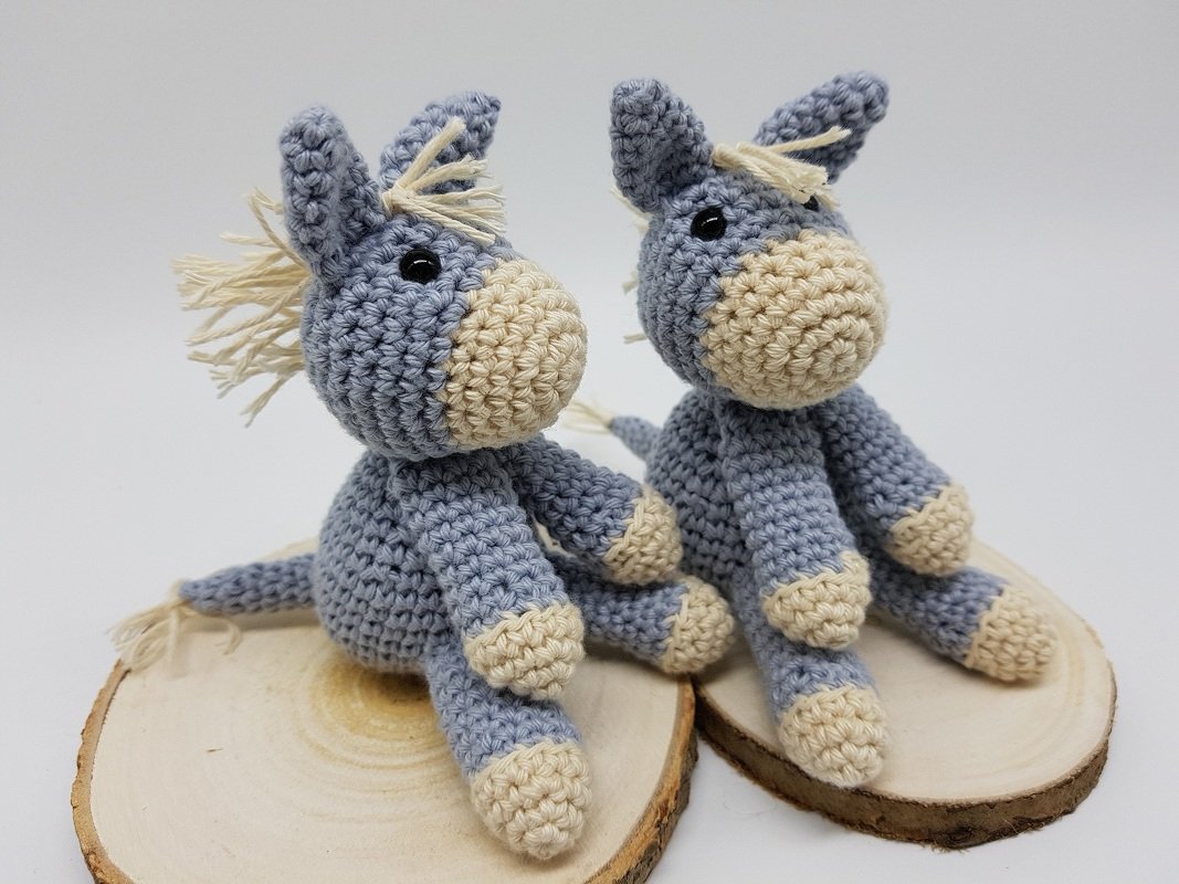 Nahaufnahme zweier sitzender gehäkelter Esel-Amigurumis mit beigen Schnauzen und Fransenmähne