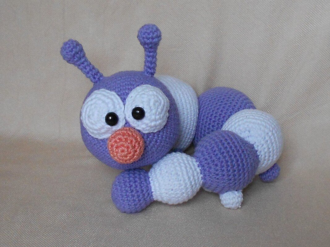 Gehäkelte Amigurumi-Raupe in violett und weiß mit orangefarbener Nase und schwarzen Augen