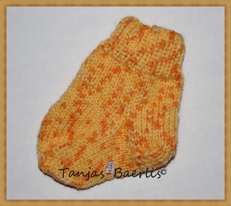 Handgestrickte Babysocke in gelb-orange Melange mit Rippenbündchen auf hellem Hintergrund.