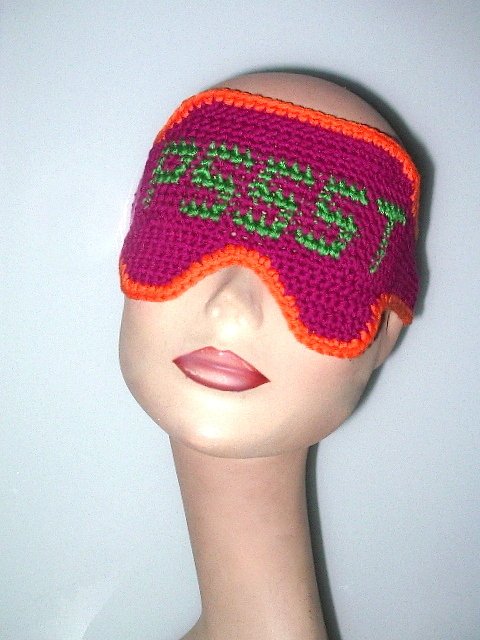 Gehäkelte Schlafmaske in Magenta mit grünem Schriftzug „PSSST“ und orangefarbener Umrandung auf Mannequin.