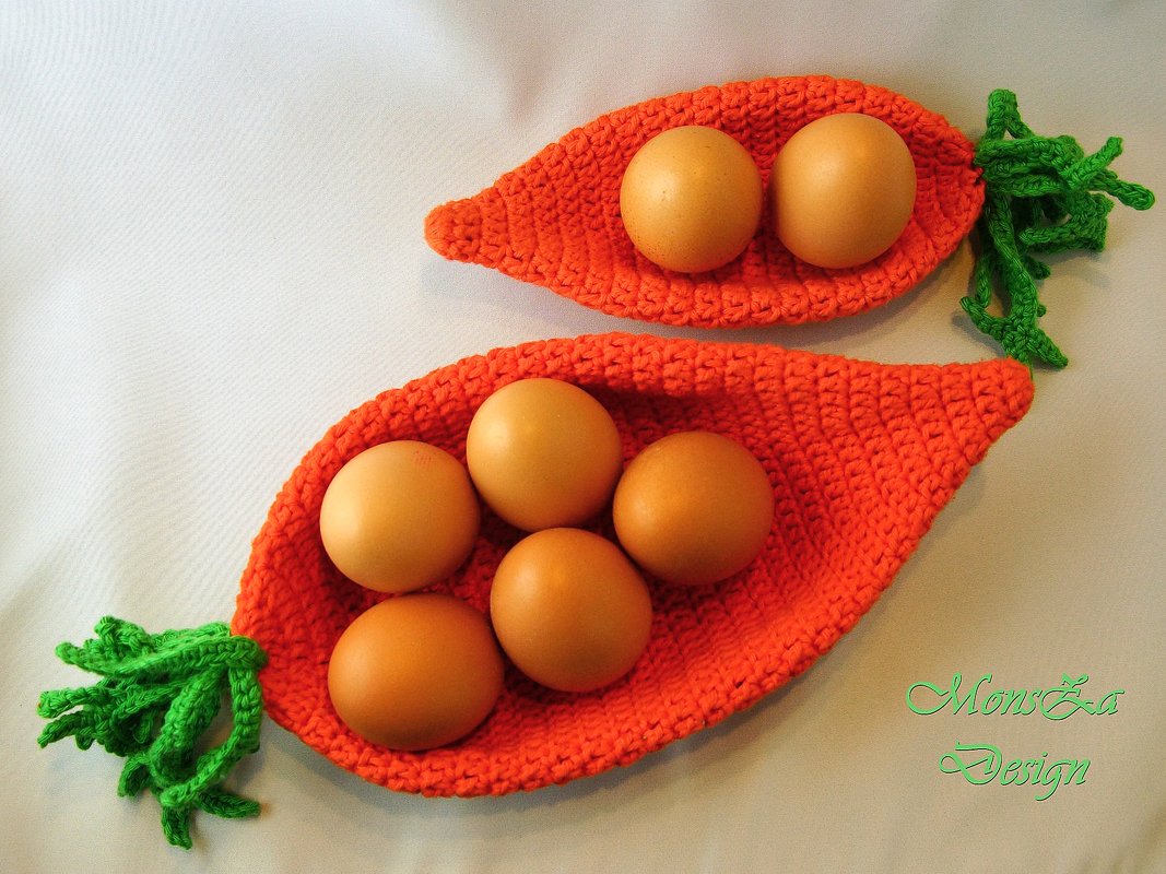 Zwei gehäkelte orange Möhrenkörbchen mit grünen Blattfransen, gefüllt mit Eiern