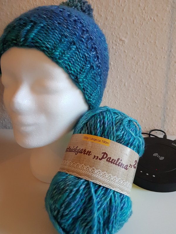 Teal gradient knit beanie with pom-pom on mannequin next to a matching yarn skein