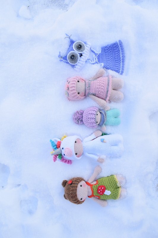 Mehrere gehäkelte Amigurumi mit unterschiedlichen Puppenkleidern auf Schnee