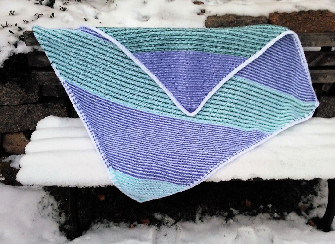 Gestricktes Baby-Dreieckstuch gestreift in Lila und Türkis auf schneebedeckter Holzbank