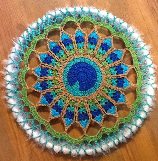 rundes gehäkeltes Mandala-Deckchen in Blau, Grün und Naturtönen mit weißem flauschigen Rand