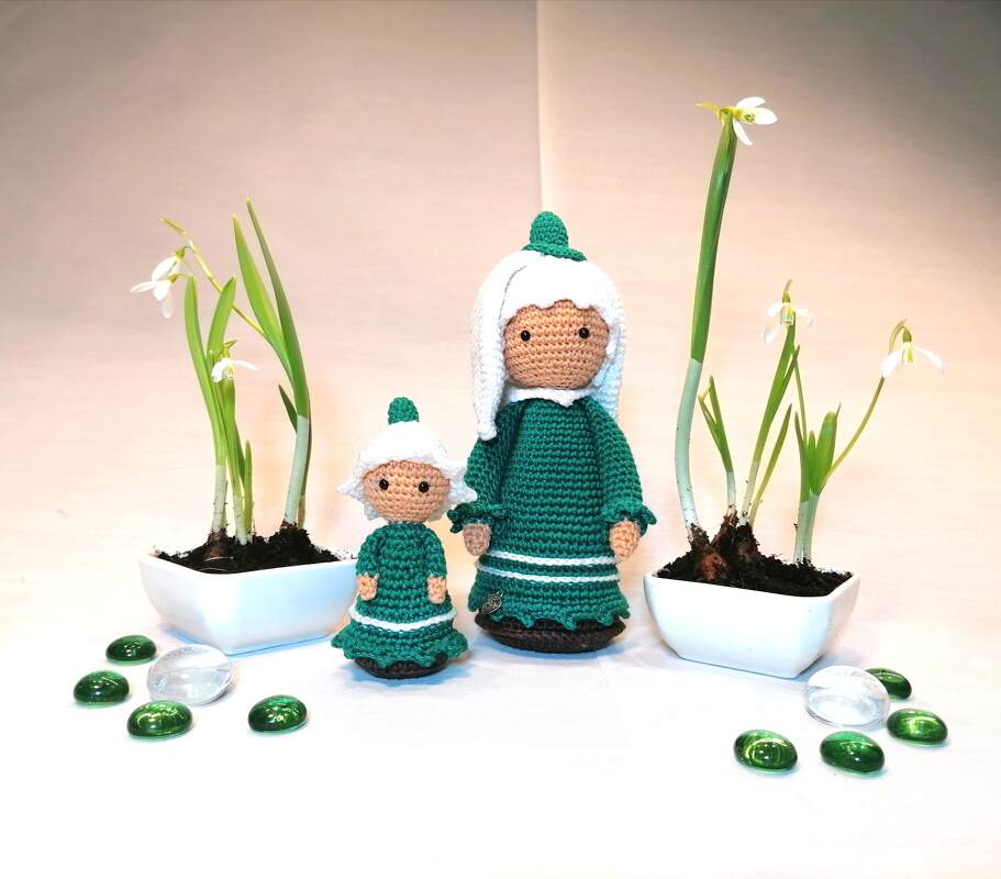 Große und kleine gehäkelte Amigurumi-Puppen in grünen Kleidern neben Schneeglöckchen