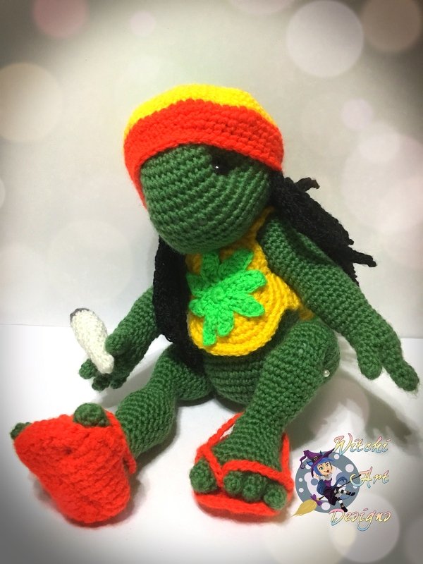 Grüne gehäkelte Amigurumi-Schildkröte mit gelb-orangefarbenem Stirnband, Blattapplikation und unterschiedlichen roten Schuhen