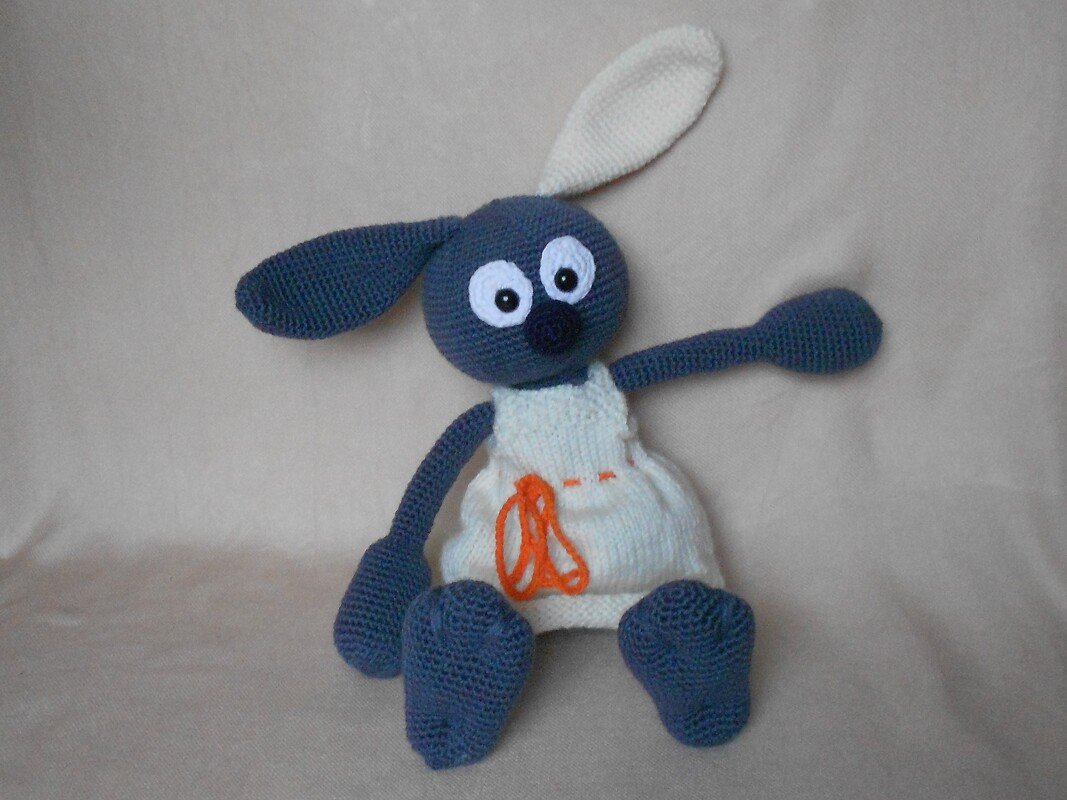 Gehäkelter blaugrauer Amigurumi-Hase mit weißem Kleid und oranger Schnürung, sitzend