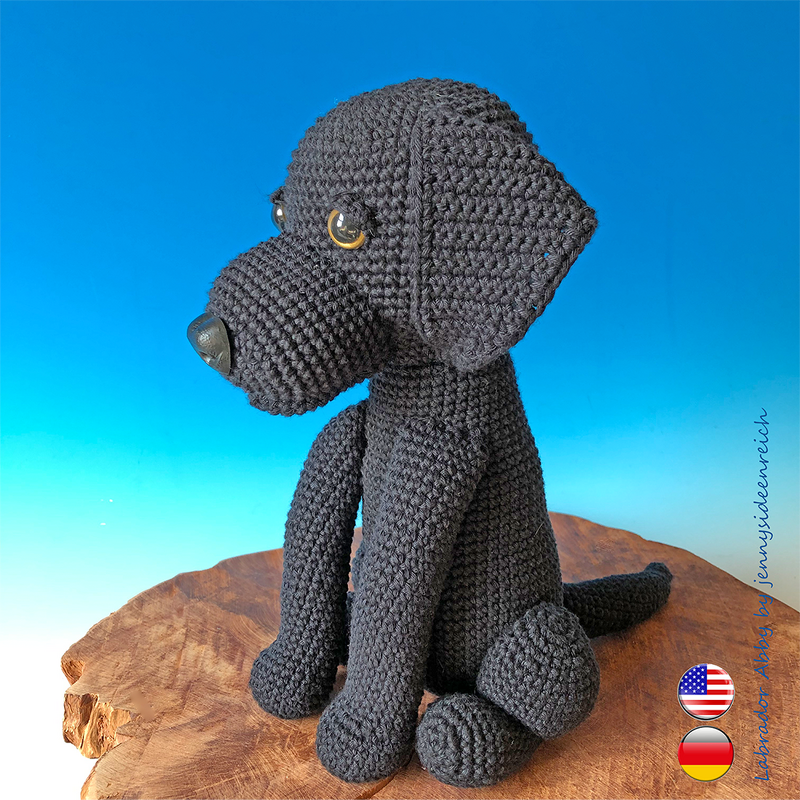 black crocheted amigurumi dog sitting on a wooden board against a blue background