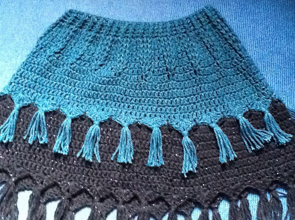 Detailansicht: gehäkelter Poncho in Türkis und Schwarz mit Quastensaum.