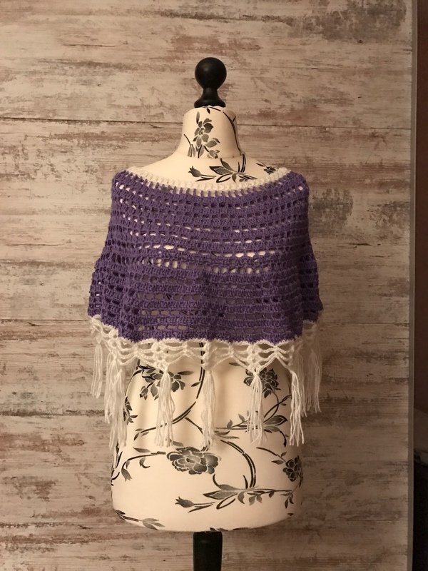 Kurzponcho mit offenem Häkelmuster in Lila und weißer Fransenborte auf einer Büste
