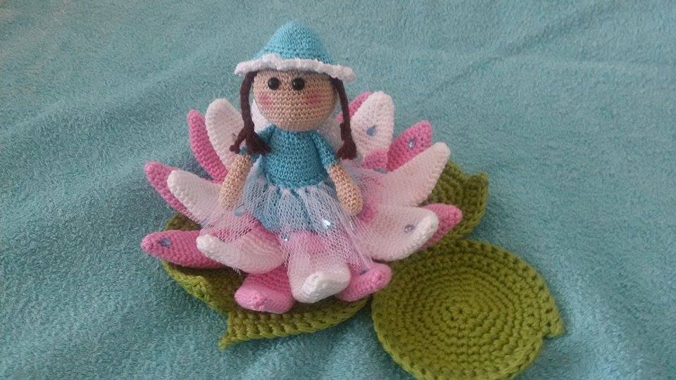 Gehäkelte Puppe mit blauem Oberteil und Tüllrock sitzt auf rosa-weißen Häkelblüten und grüner Blattunterlage