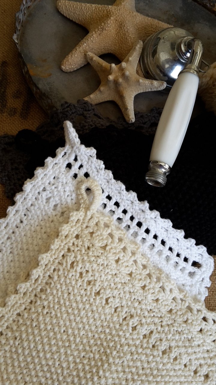 Zwei handgearbeitete Tücher, weiß und beige, mit Lochmuster und Aufhängeschlaufen neben maritimen Dekoelementen.