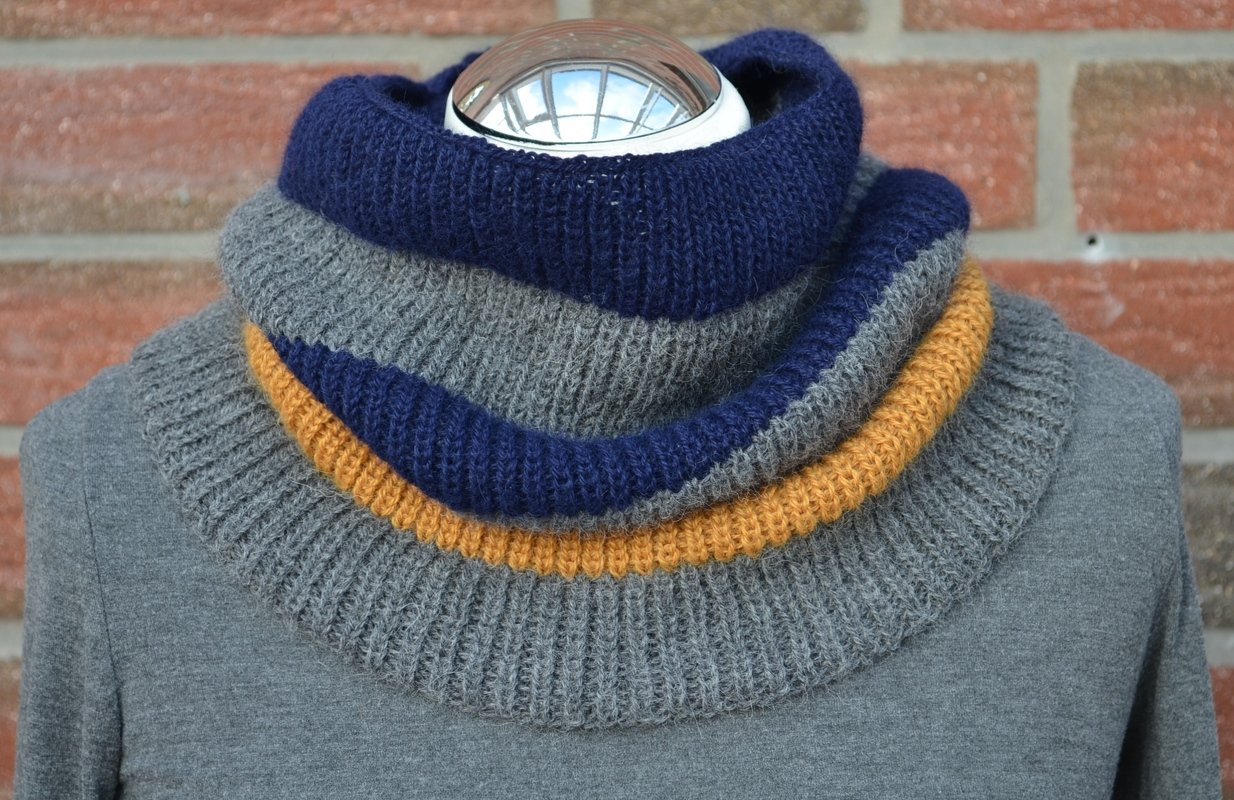 Gestrickter Loop-Schal mit blauen, grauen und senfgelben Streifen auf einer Schaufensterpuppe