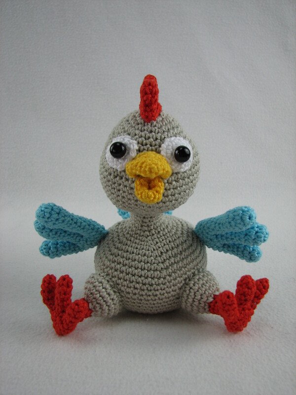 Gehäkeltes Amigurumi‑Huhn grau mit rotem Kamm, gelbem Schnabel und blauen Flügeln