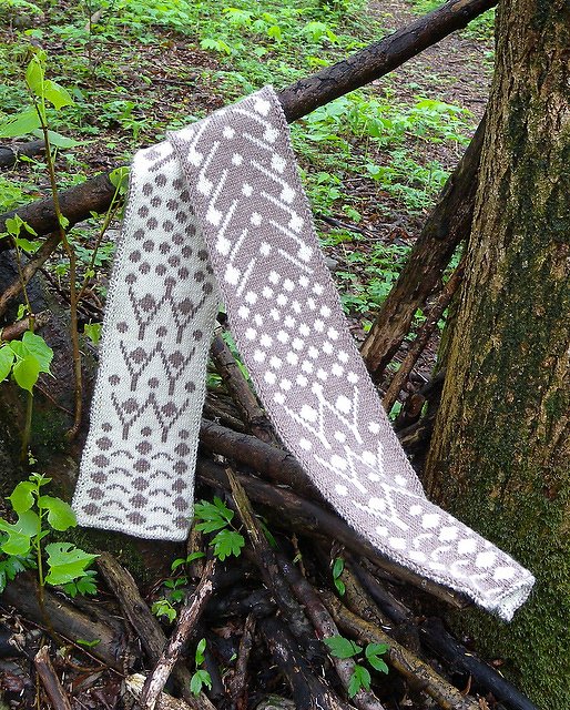 Gestrickter Schal in Hellgrau und Braun mit Jaquardmuster über einem Ast im Wald