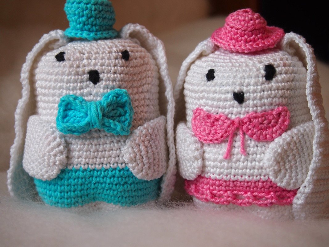 Two white crocheted amigurumi bunnies with teal and pink accessories