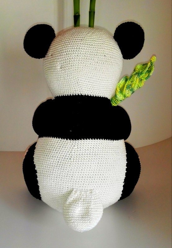 Rückansicht eines gehäkelten schwarz-weißen Pandas mit kleinem weißem Schwanz und grünen Bambuselementen.