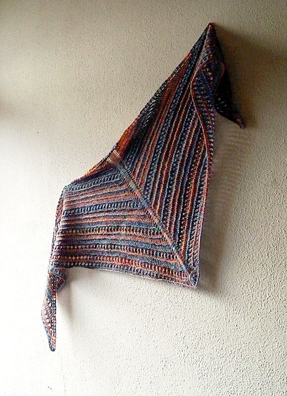 Gestricktes Dreieckstuch in Blau-, Grau- und Orangetönen, an einer Wand aufgehängt