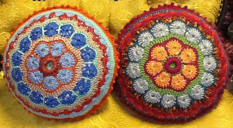 Nahaufnahme zweier bunter, runder Häkelkissen mit konzentrischen Blütenmustern