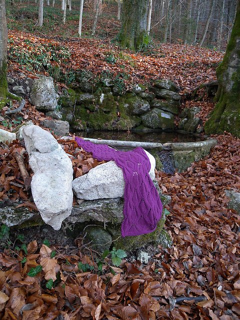 Lila gestrickter Schal mit Rautenmuster auf Steinen im Herbstwald