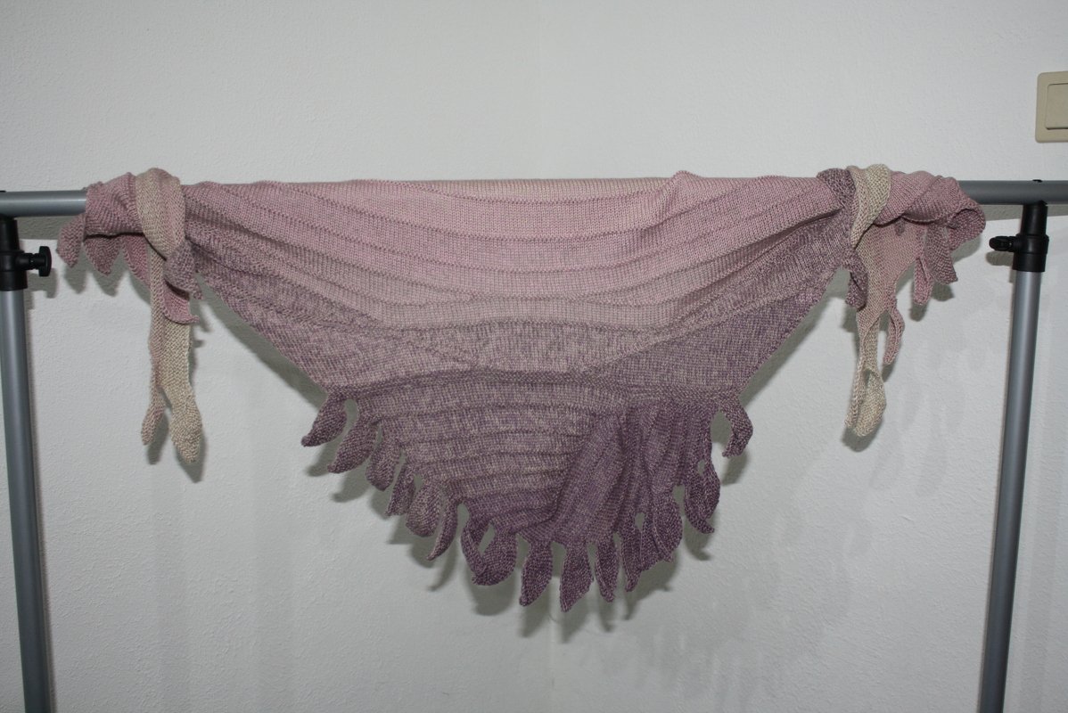Gestricktes Dreieckstuch in Rosa- bis Violettverlauf mit gezackter Kante, aufgehängt