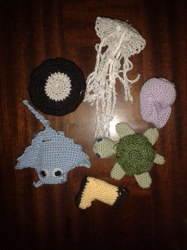 Gehäkelte Meerestiere und Kinderspielzeuge (Qualle, Rochen, Schildkröte, Schnecke) auf dunklem Holztisch