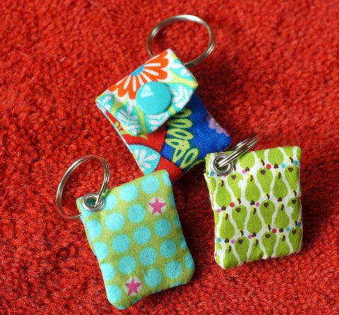 Nahaufnahme von drei gepolsterten Schlüsselanhänger-Täschchen aus gemustertem Stoff auf rotem Untergrund