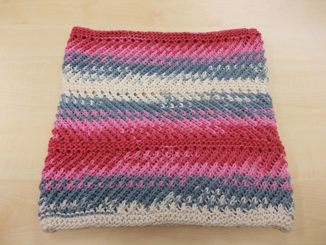 Gefalteter gestrickter Loop mit diagonalen Streifen in Rot, Rosa, Grau und Creme auf hellem Holz