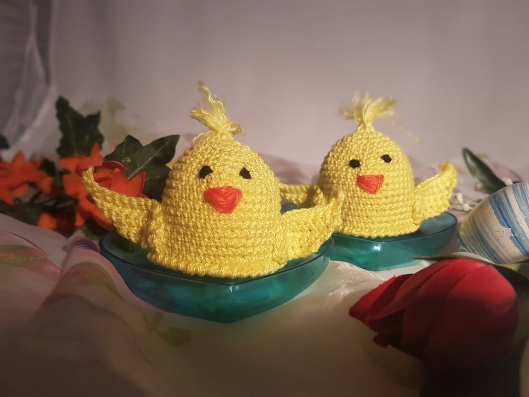 Zwei gelbe gehäkelte Küken-Eierwärmer in türkisfarbenen Schalen mit Blumen-Dekoration