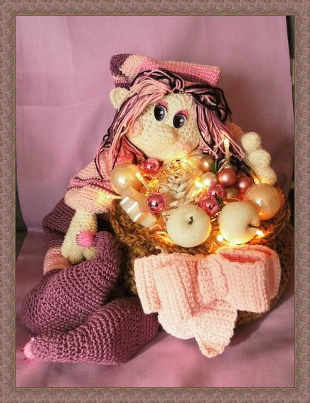 Gehäkelte Puppe in Rosa und Lila hält Korb mit Christbaumkugeln und Lichterkette