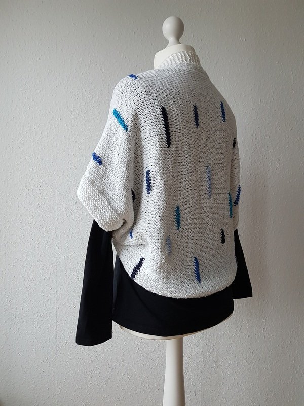Weißer gestrickter Seelenwärmer mit blauen Einstrickungen an Schaufensterpuppe