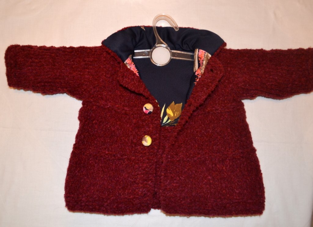 Gestrickte Babyjacke in dunklem Rot mit zwei Knöpfen und gemustertem Innenfutter auf Kleiderbügel
