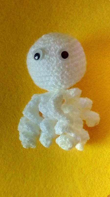 Weiß gehäkelter Amigurumi-Oktopus mit spiralförmigen Tentakeln auf gelbem Hintergrund