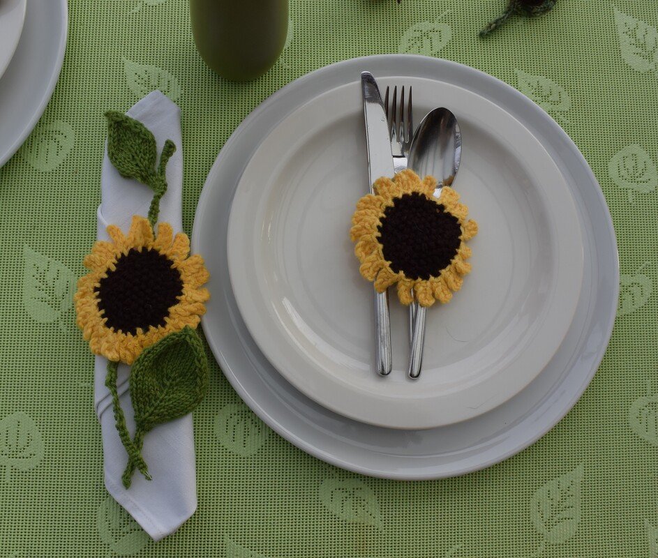 Nahaufnahme eines gehäkelten Sonnenblumen-Serviettenhalters mit grünem Blatt auf weißem Teller
