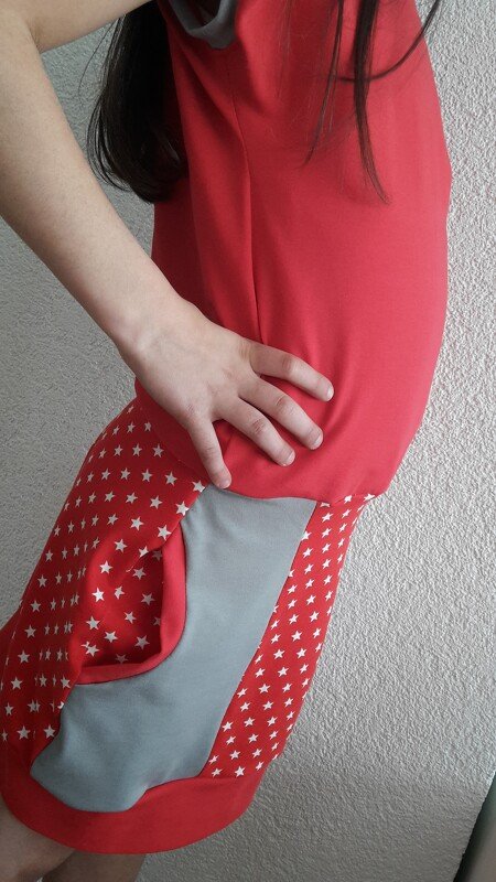 Seitliche Ansicht eines roten Kinderkleids mit Sternchenrock und hellgrauer Seitentasche, Hand auf Hüfte