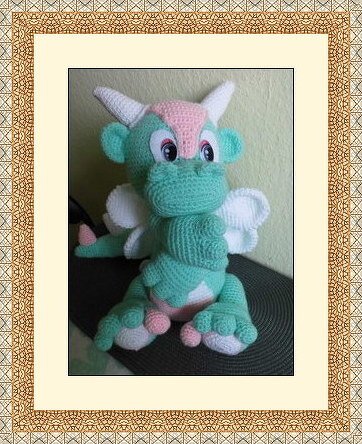 Gehäkelter Amigurumi-Drache in Mintgrün mit rosa und weißen Akzenten, sitzend.